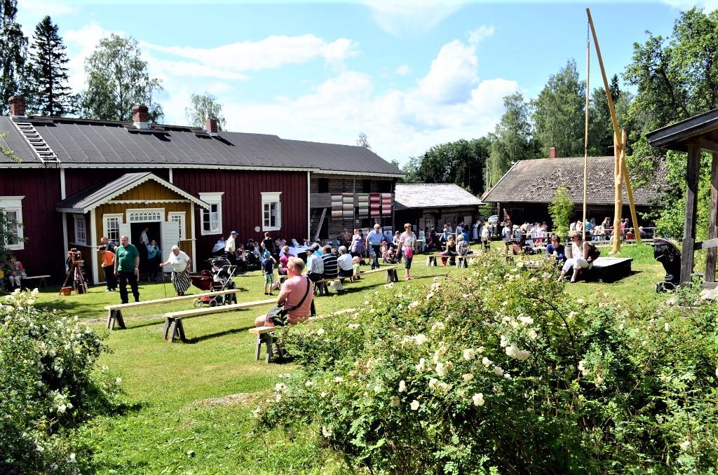 Ihmisiä museon pihapiirissä kesäpäivänä, punainen päärakennus taustalla